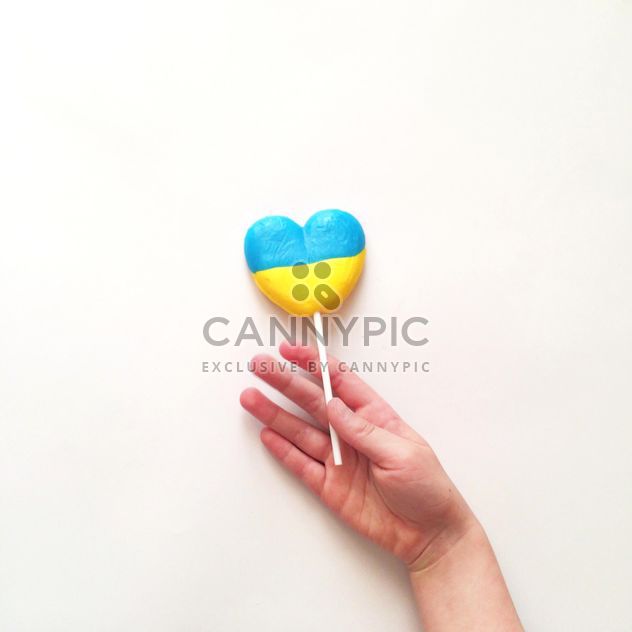 Child's hand and lollipop in colors of Ukrainian flag on white background - бесплатный image #329299