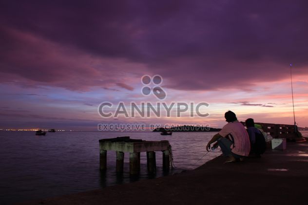 Fishermen sitting on waterfront at sunset - бесплатный image #348949