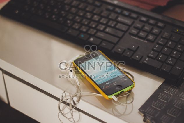 Smartphone with earphones lying on work place next to black keyboard - Free image #343509