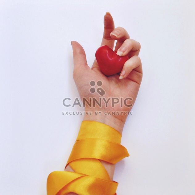 Red heart in female hand with yellow ribbon - бесплатный image #345879