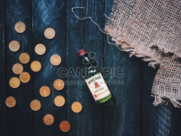 Small bottle of whiskey and coins on wooden background - бесплатный image #348639