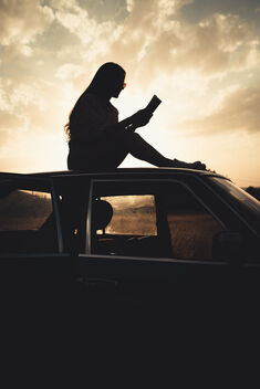 A woman sitting on a car and reading the book in nature at the sunset. - image #475289 gratis